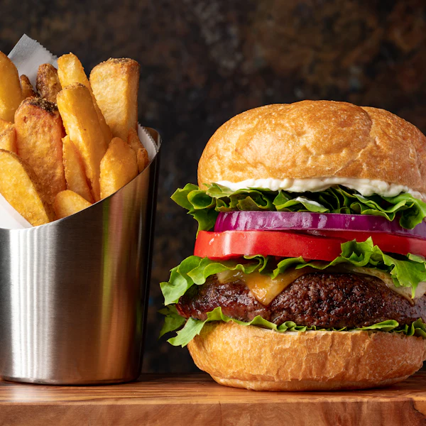 Un cheeseburger à la tomate et à l’oignon rouge à côté d’un cornet de frites