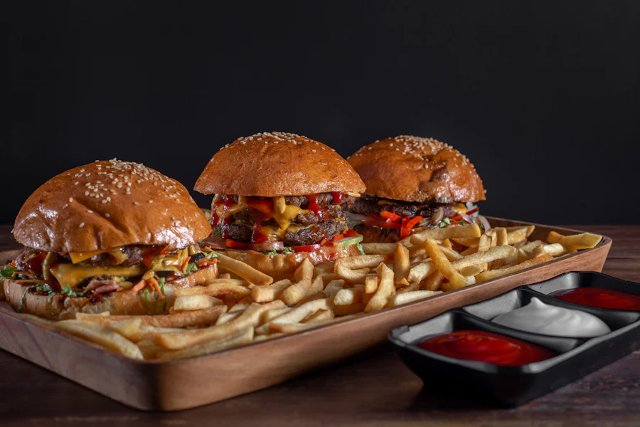 Trois cheeseburgers sur un plateau en bois garni de frites et de sauces